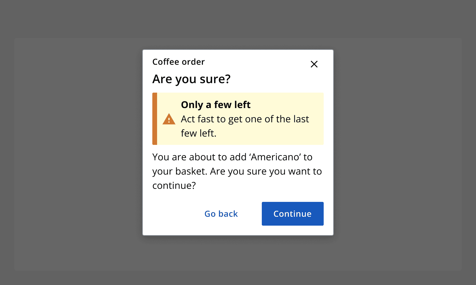 An example dialog for a coffee order asking if the user is sure they want to continue adding the product 'Americano' to their basket. It contains a warning alert that says 'Only a few left'.